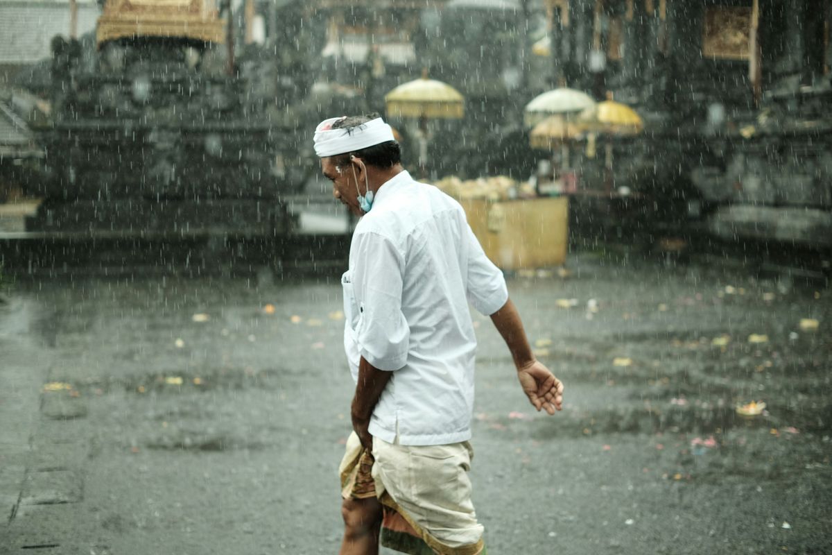 Ein Mann geht bei Regen über einen Tempelvorplatz auf Bali